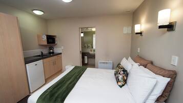 A hotel room with a bed, a microwave, a sink, and a mirror.