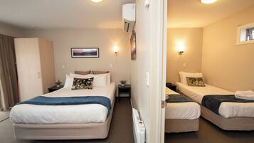 A hotel room with two beds, a nightstand, a wall-mounted air conditioner, a framed picture, and a window.