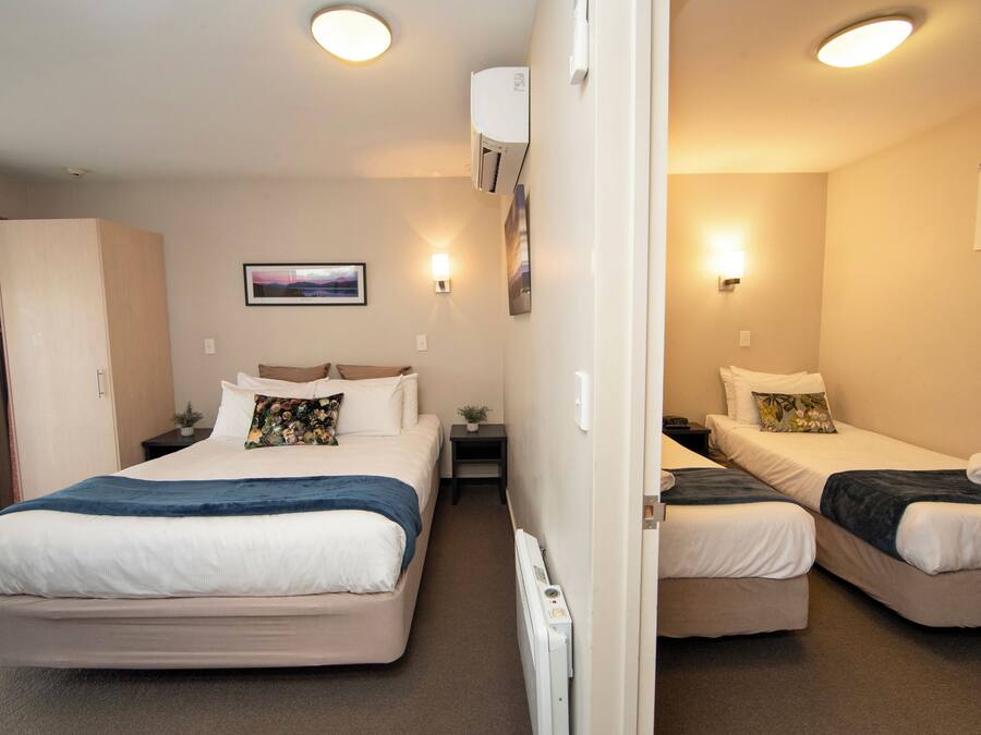 Quarto de hotel com duas camas, uma mesinha de cabeceira, ar condicionado fixado na parede, um quadro emoldurado e uma janela.