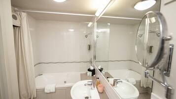 A modern bathroom with a bathtub, two sinks, a large mirror, and a shower.