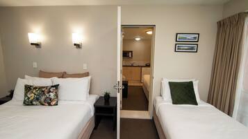 A hotel room with two beds, a small table with a plant, a door leading to a bathroom, and a view of the bathroom through the door.