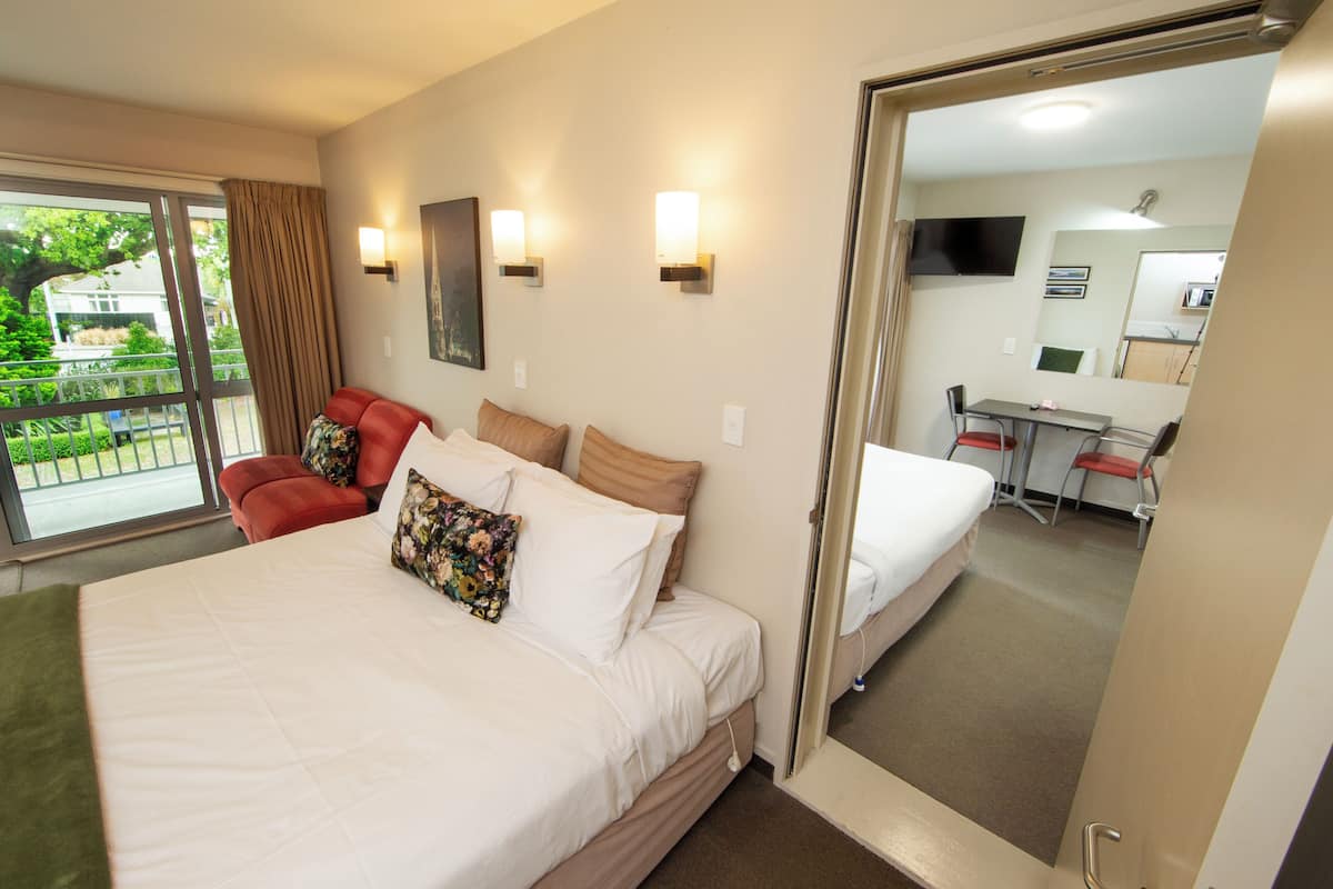 A hotel room with a large bed, a red chair, a desk, and a view of the outdoors.