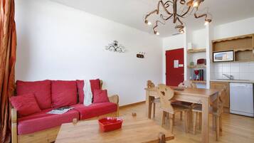 A compact living space with a red sofa, wooden dining table, and a kitchen area with a microwave.