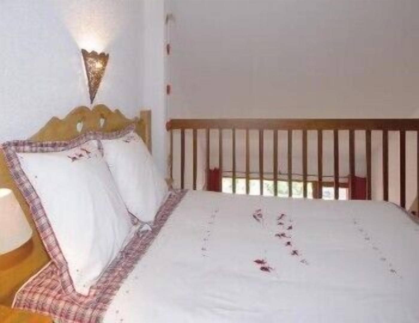 A bedroom with a wooden headboard, a bed with white bedding, and a wall-mounted light fixture.