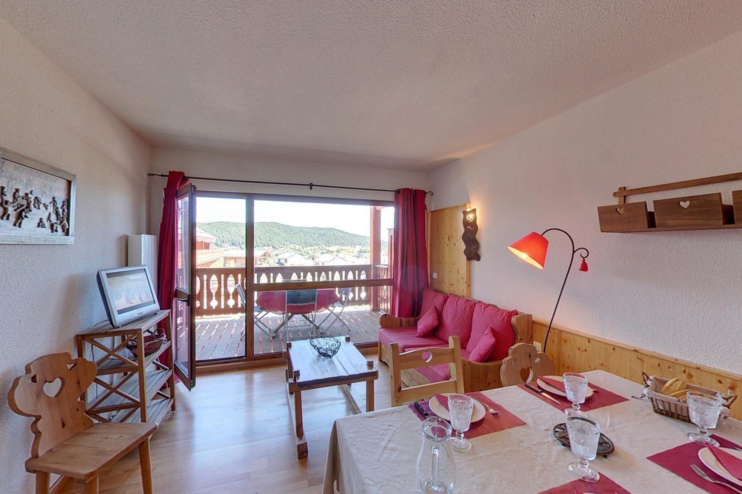 Une pièce confortable avec un balcon, un canapé, une table dressée pour le repas et un téléviseur posé sur un meuble.