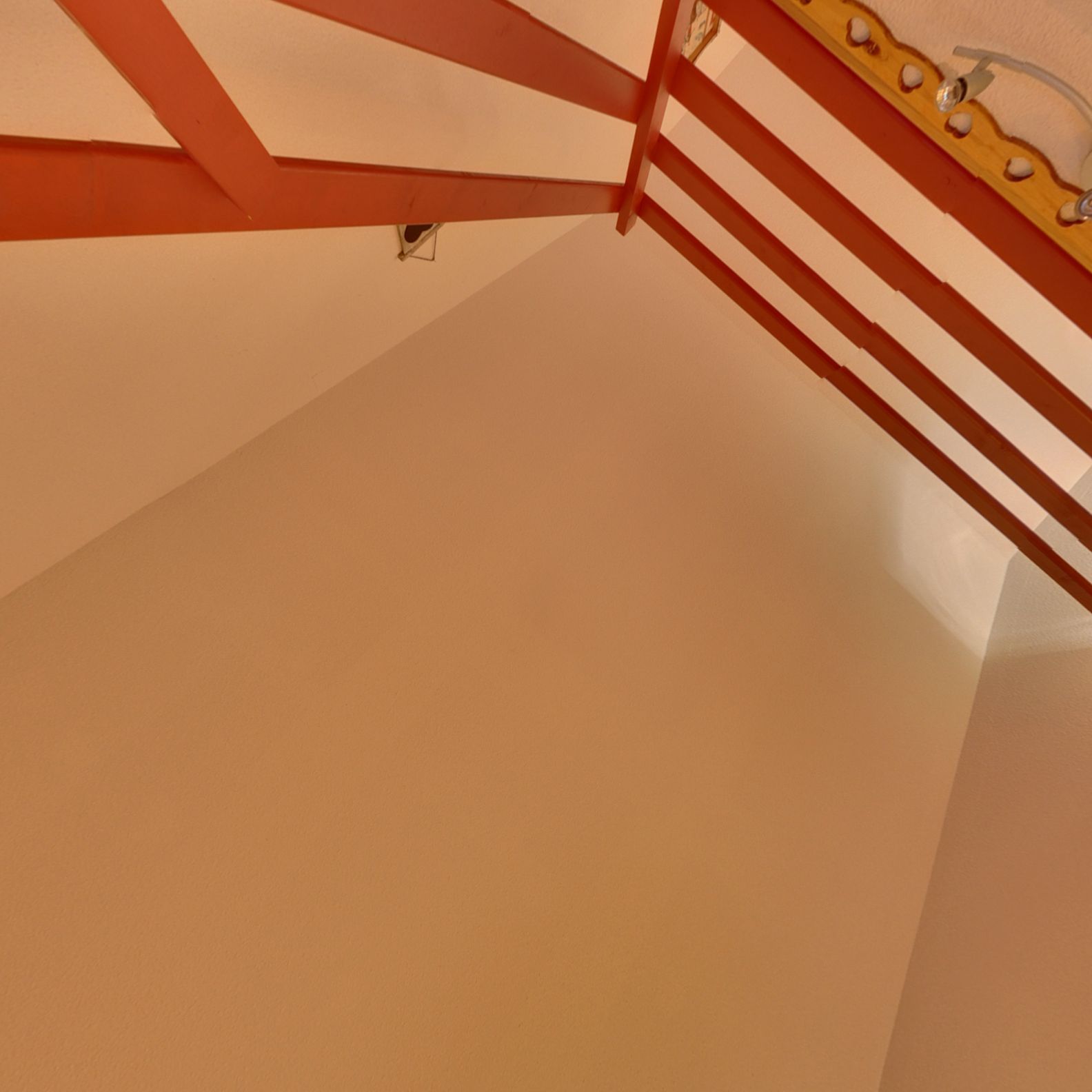 Rincón de una habitación con techo blanco y una estructura metálica roja, posiblemente parte de una escalera o soporte.