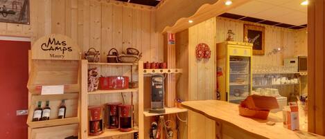 Un interior acogedor y rústico con estantes de madera que exhiben botellas de vino y máquinas de café, una barra con una cafetera, y un letrero que dice "Mas Camps Maury".