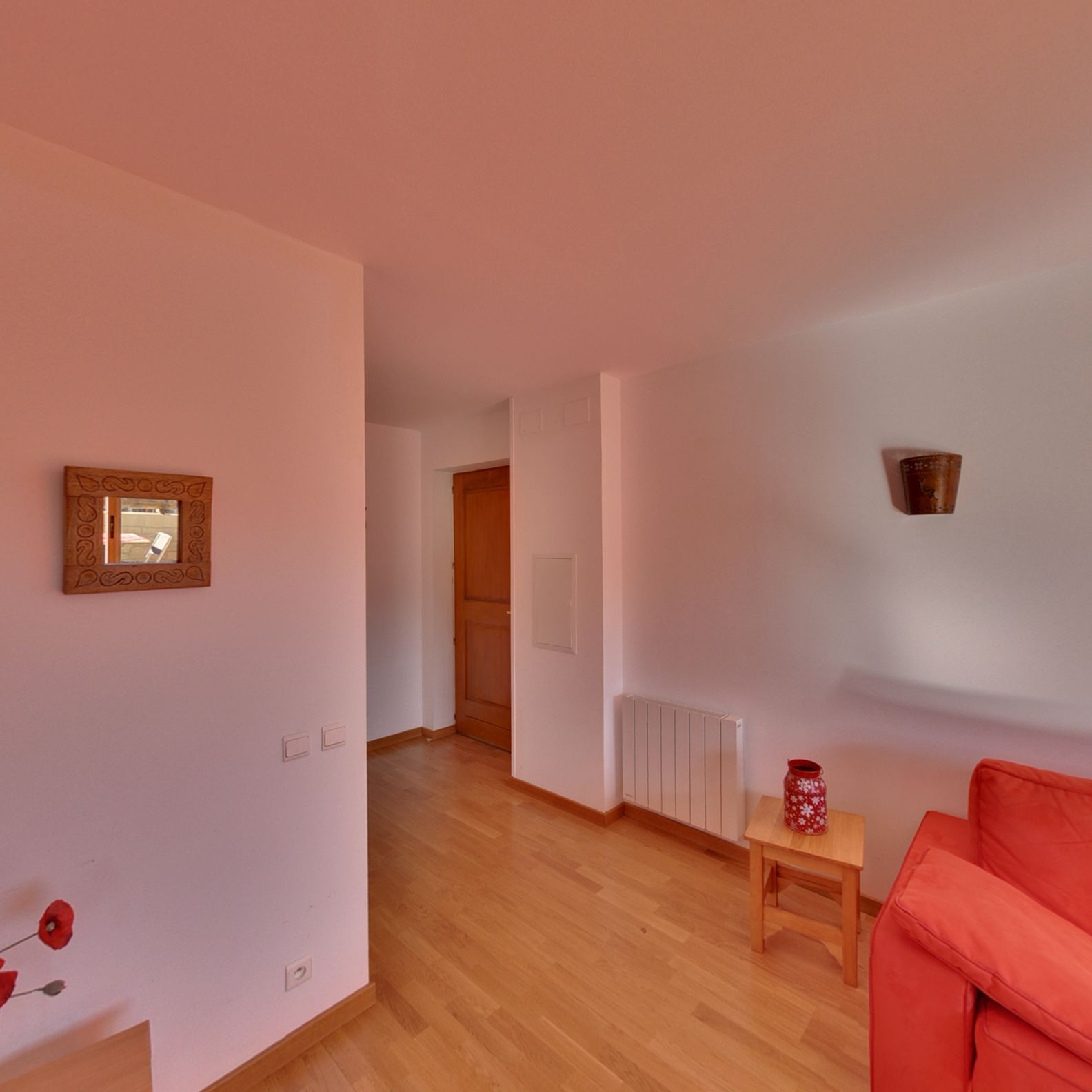 A spacious room with wooden flooring, a red sofa, a small table, and a radiator.