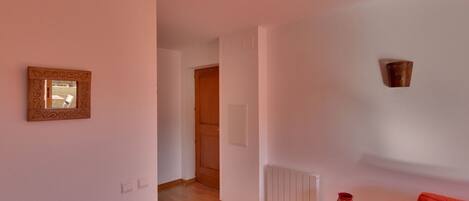 A spacious room with wooden flooring, a red sofa, a small table, and a radiator.