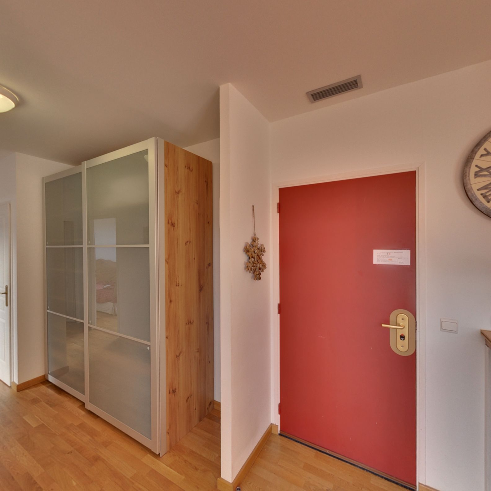 A room with a wooden wardrobe, a red door, and a clock on the wall.
