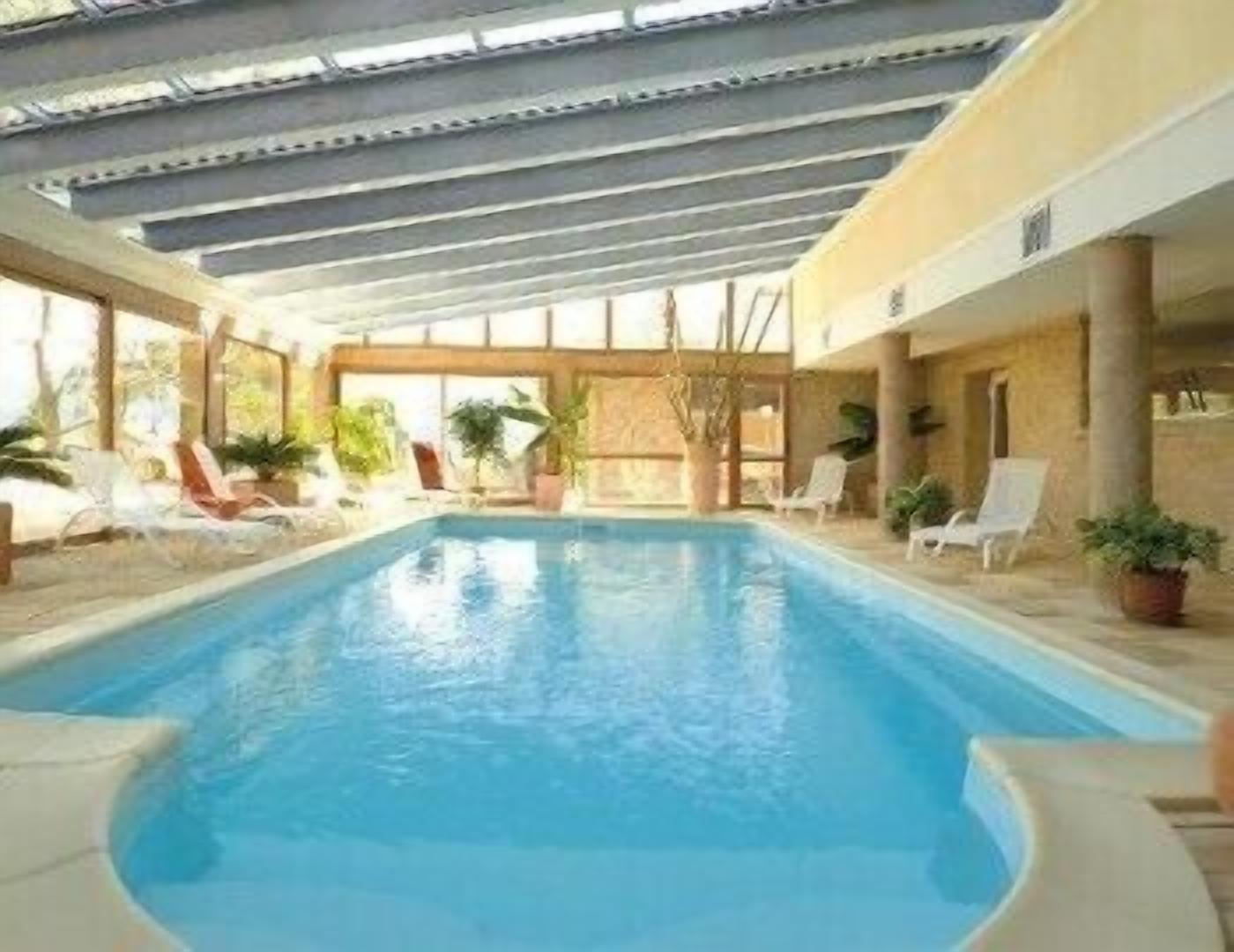 An indoor swimming pool with lounge chairs and potted plants.