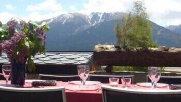 Area pranzo all'aperto con tavoli apparecchiati per due, con vista su un paesaggio montuoso.