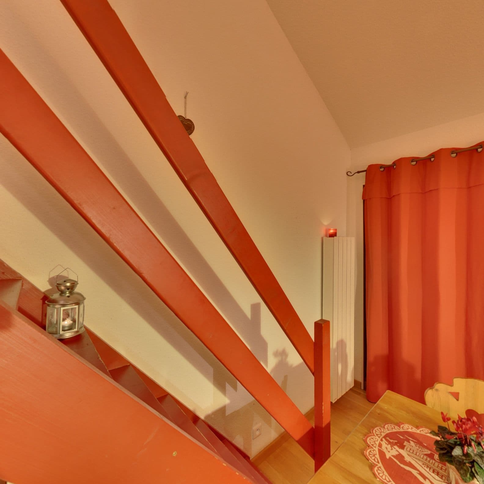 Una escalera con barandillas rojas, un farol, un radiador y una cortina roja.