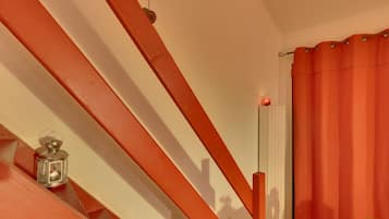 Una escalera con barandillas rojas, un farol, un radiador y una cortina roja.