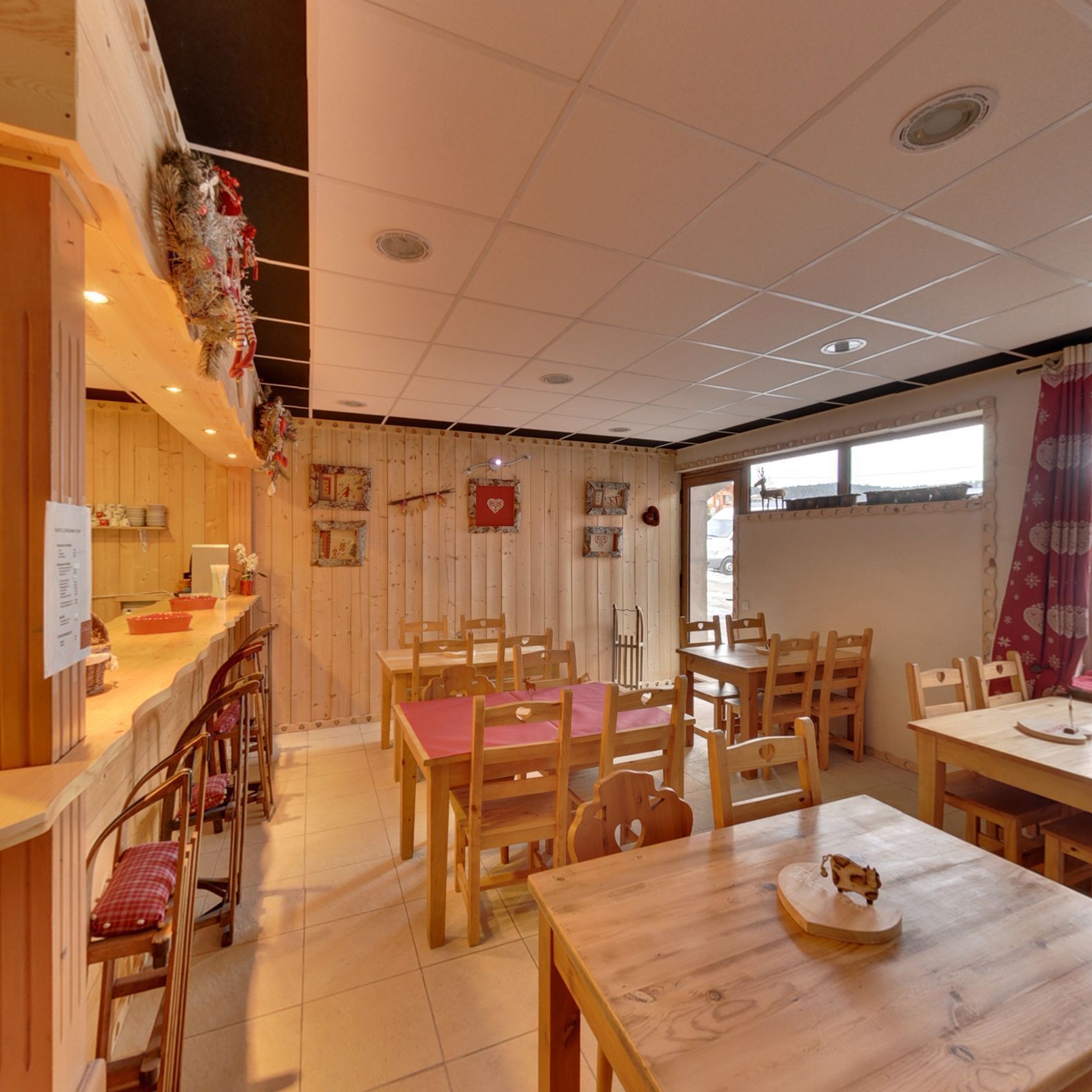 A cozy dining area with wooden tables and chairs, a counter with a menu, and a window with a view.