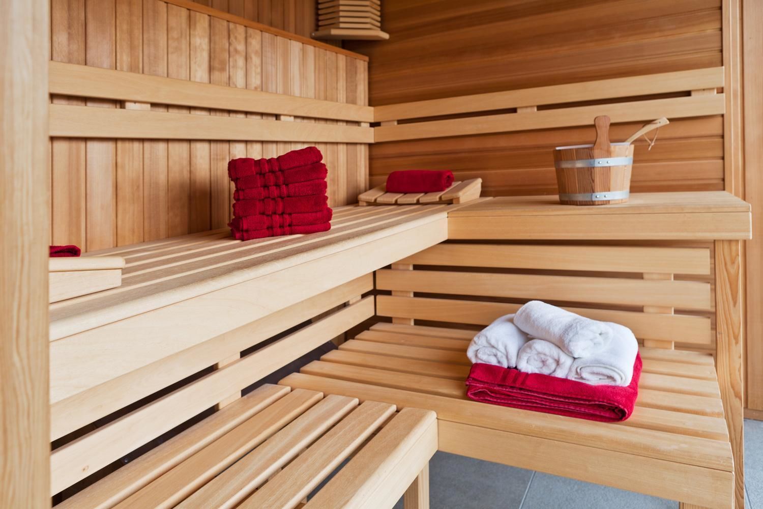 A sauna with wooden benches and shelves, towels, and a bucket.