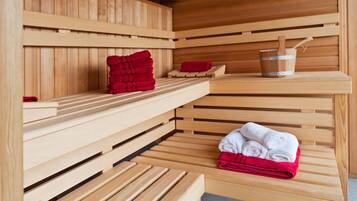 A sauna with wooden benches and shelves, towels, and a bucket.