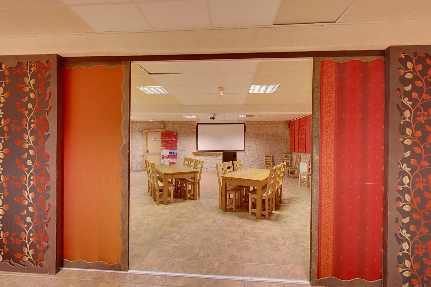 A conference room with two wooden tables and chairs, a projector screen, and a stone wall.