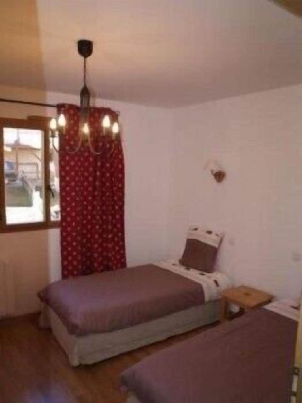 Una habitación pequeña con cama individual, techo de madera, ventana con cortinas y mesita de noche con lámpara.