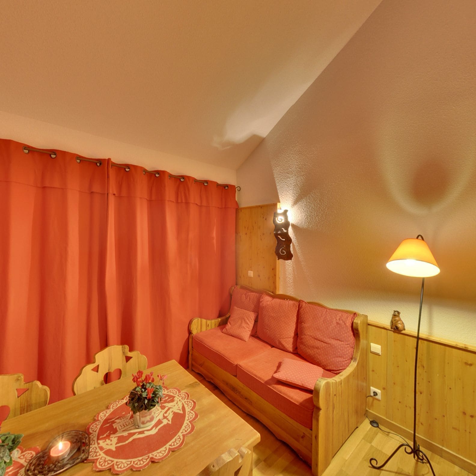 A cozy room with a wooden sofa, a dining table with a floral centerpiece, and a lamp.