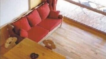 Un divano rosso con cuscini, un tavolino in legno e una finestra che si affaccia su un'area pavimentata.