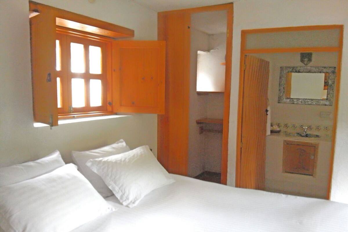 Ein Schlafzimmer mit Bett, zwei Kissen, einem Holzschrank, einem Spiegel und einer Badezimmertür.