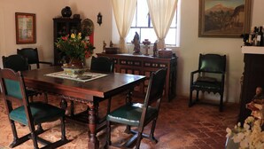 A dining room with a wooden table, green upholstered chairs, a vase of flowers, and a painting on the wall.