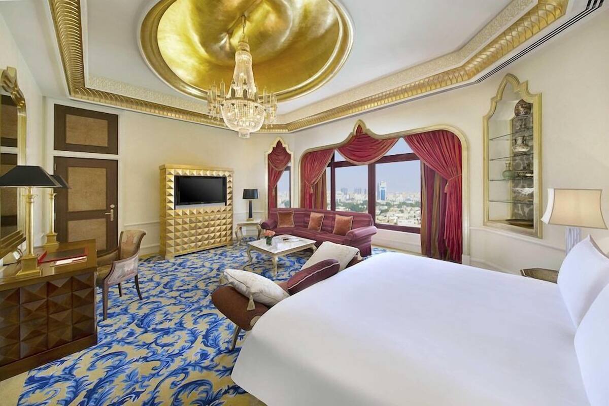 A hotel room with a large bed, a sofa, a TV, and a chandelier.
