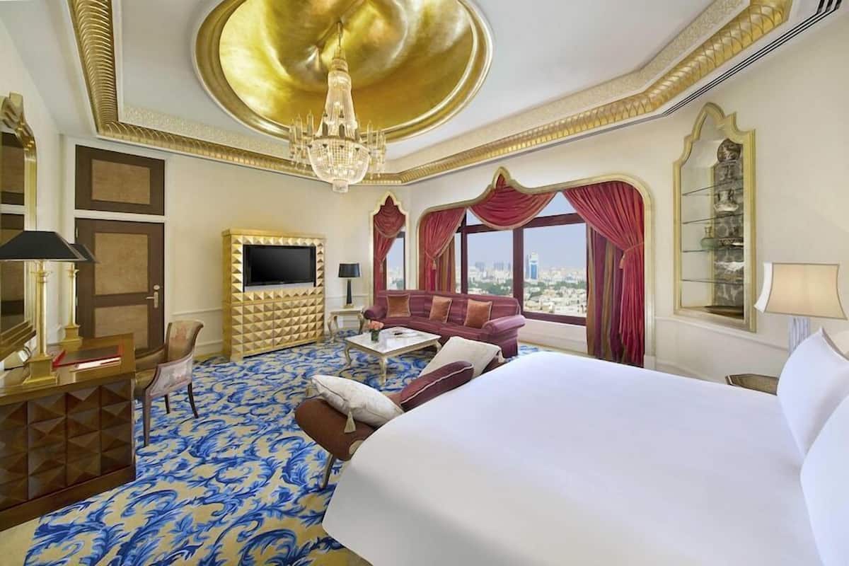 Una habitación de hotel con una cama grande, un sofá, un televisor y una araña.
