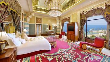 A luxurious hotel room with a large bed, a red sofa, a chandelier, and a view of the sea.
