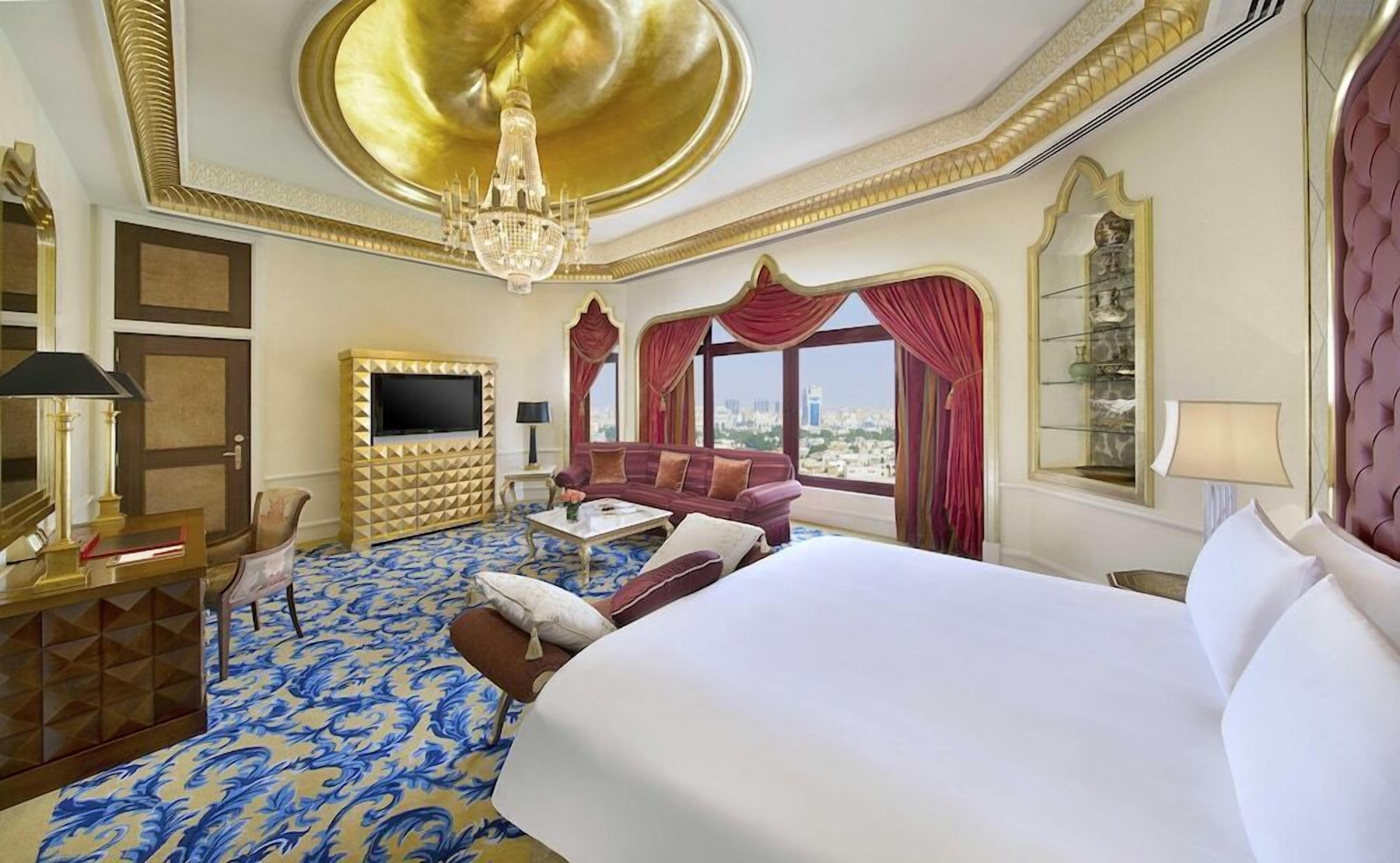 A hotel room with a large bed, a sofa, a TV, and a chandelier.