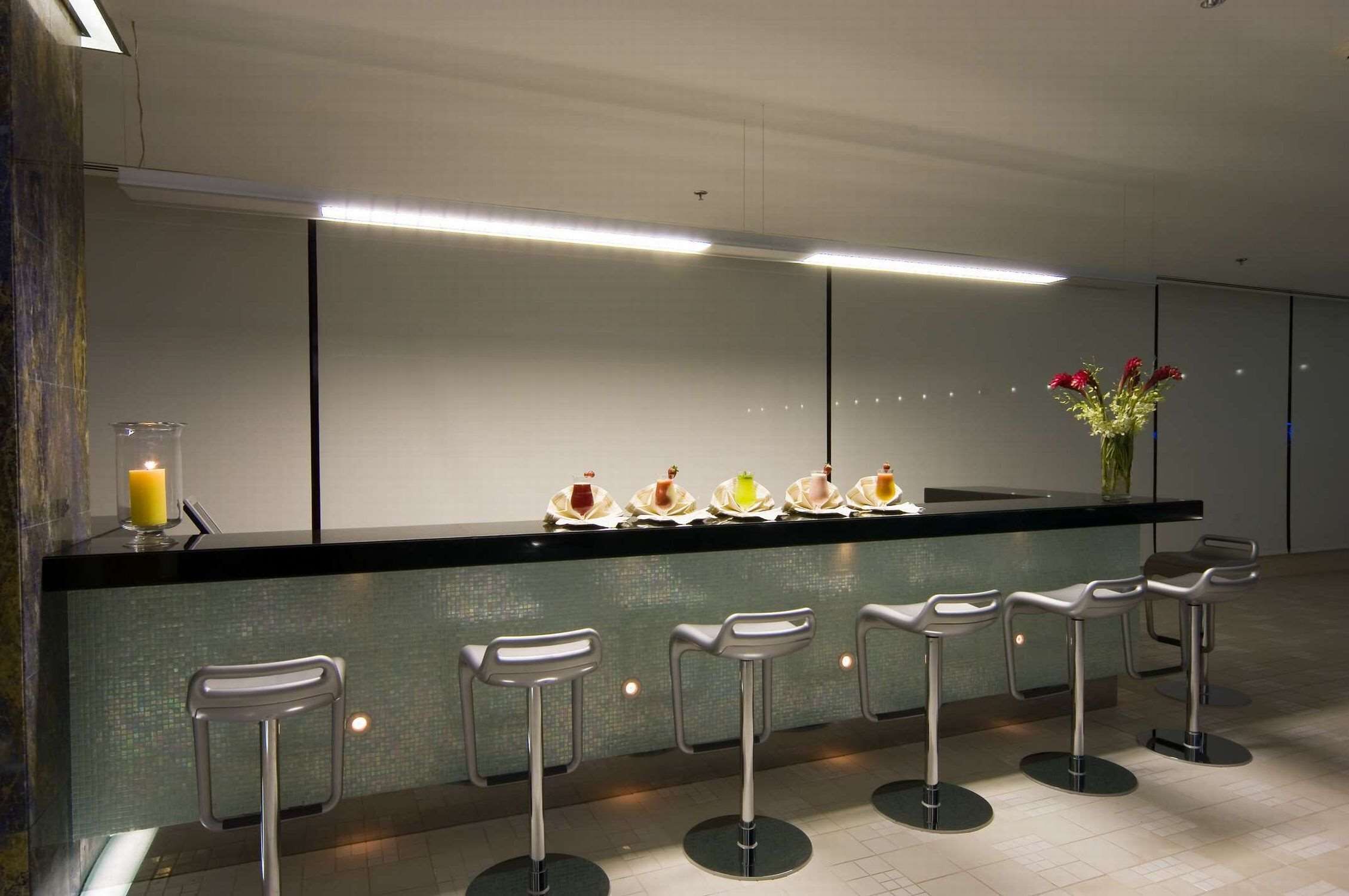 Un área de bar moderna con una encimera negra, varios taburetes y un florero con flores.