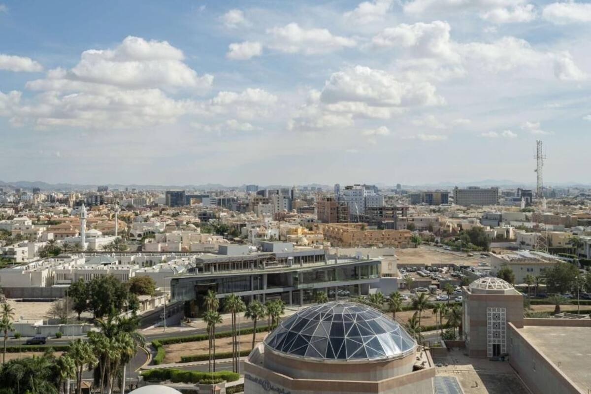 A cityscape with a prominent dome structure in the foreground, surrounded by modern buildings and palm trees.
