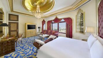 Ein luxuriöses Hotelzimmer mit einem großen Bett, einem an einer goldenen geometrischen Wand montierten Fernseher, einer Kristallleuchtre und einem Blick auf die Stadt durch große Fenster.