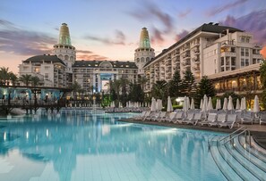 A hotel with a large swimming pool, lounge chairs, and umbrellas. - Delphin Diva Premiere Hotel - All Inclusive (Antalya)