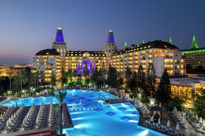 A large hotel with a swimming pool, multiple balconies, and a well-lit facade. - Delphin Diva Premiere Hotel - All Inclusive (Antalya)