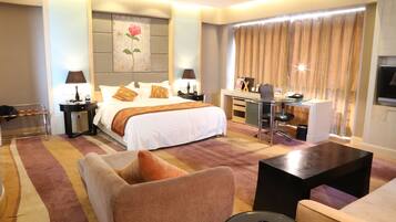 A hotel room with a large bed, a desk, a chair, a sofa, and a television.