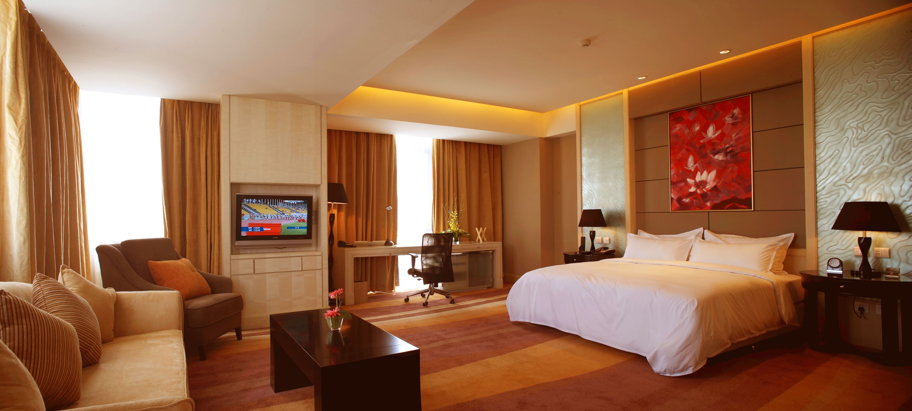A hotel room with a large bed, a desk with a computer, a TV, and a sofa.