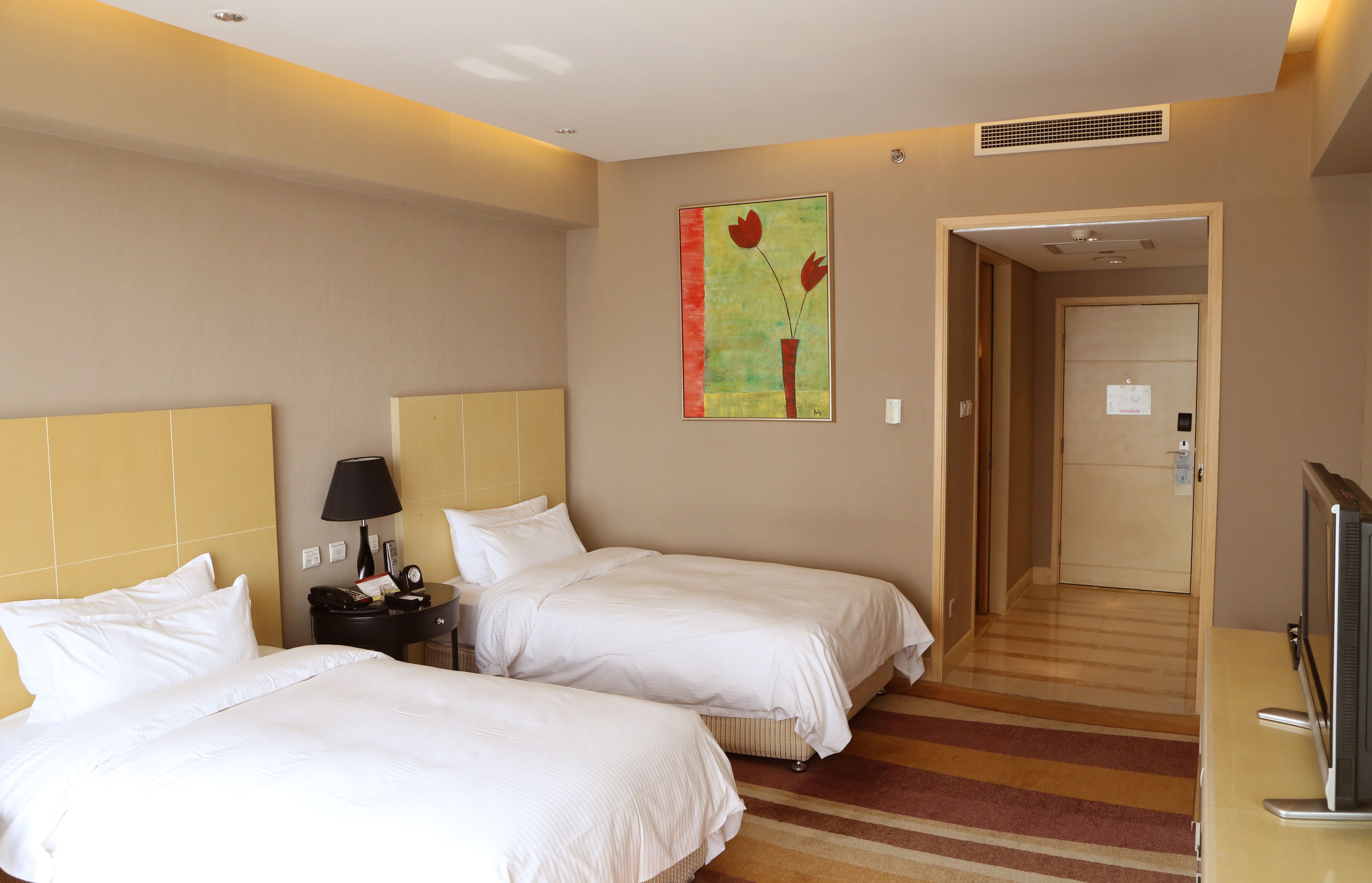 A hotel room with two beds, a nightstand, a lamp, a TV, and a painting on the wall.
