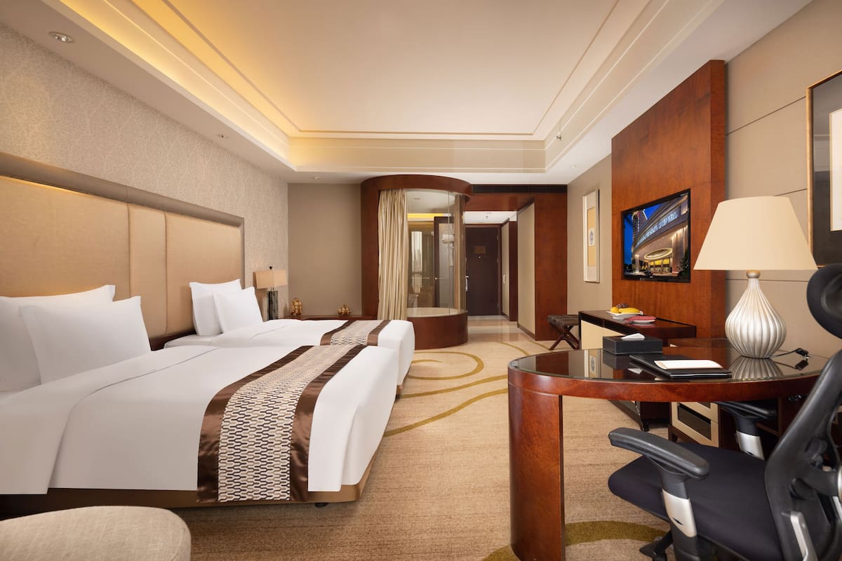 A hotel room with a large bed, a desk, a chair, a TV, and a lamp.