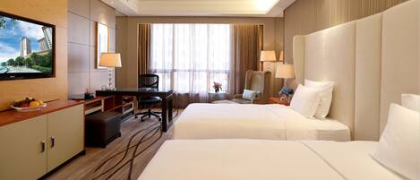A hotel room with two beds, a desk, a TV, and a large window with curtains.