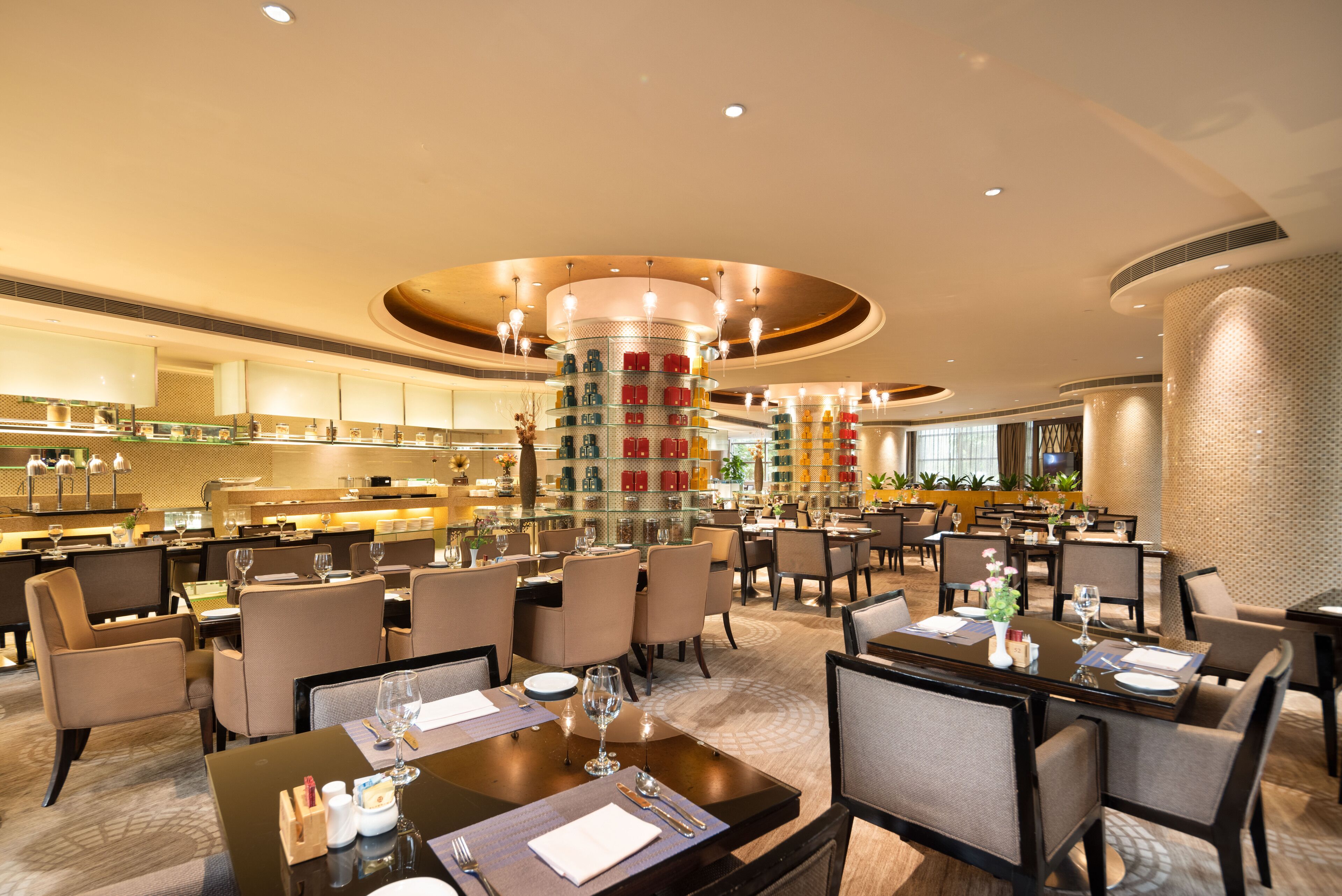 A hotel lobby with multiple dining areas, a central decorative column, and a well-lit ceiling.