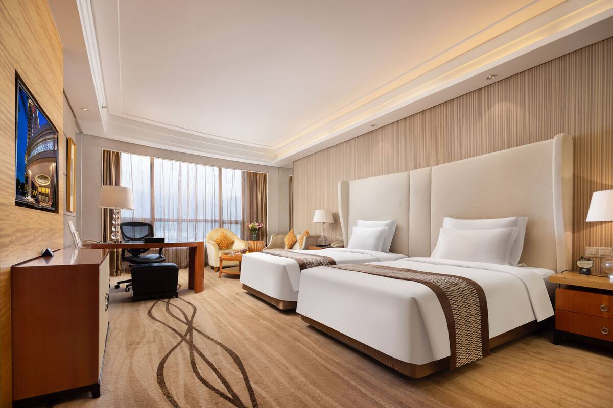 A hotel room with a large bed, a desk, a chair, and a TV.