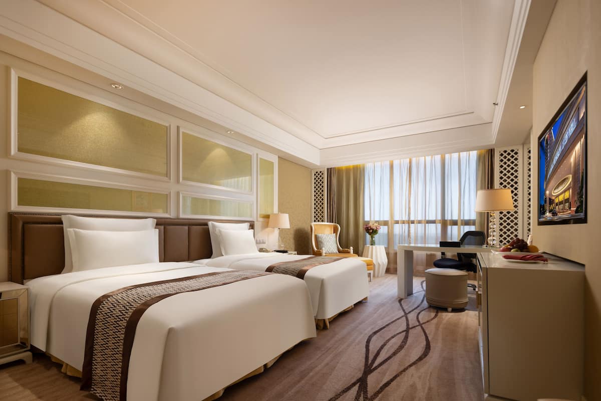 A hotel room with two beds, a desk, and a chair.