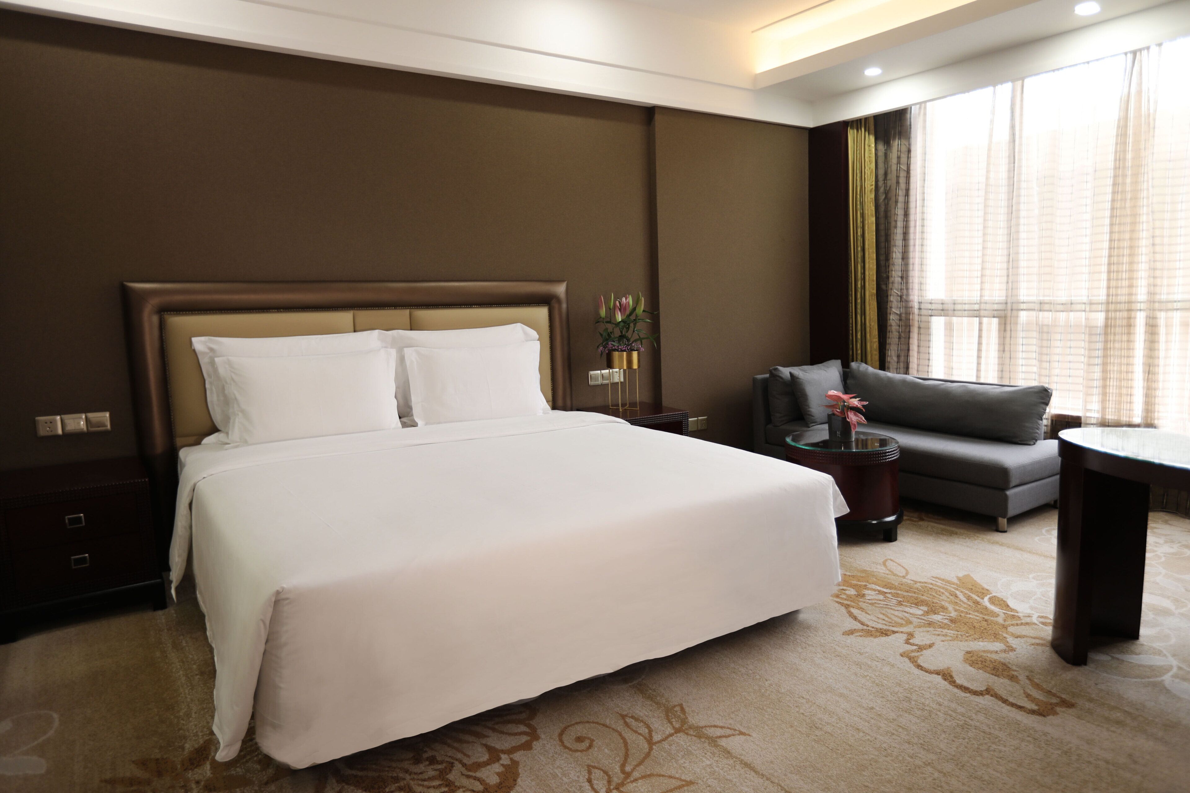 A hotel room with a large bed, a sofa, a small table, and a nightstand.