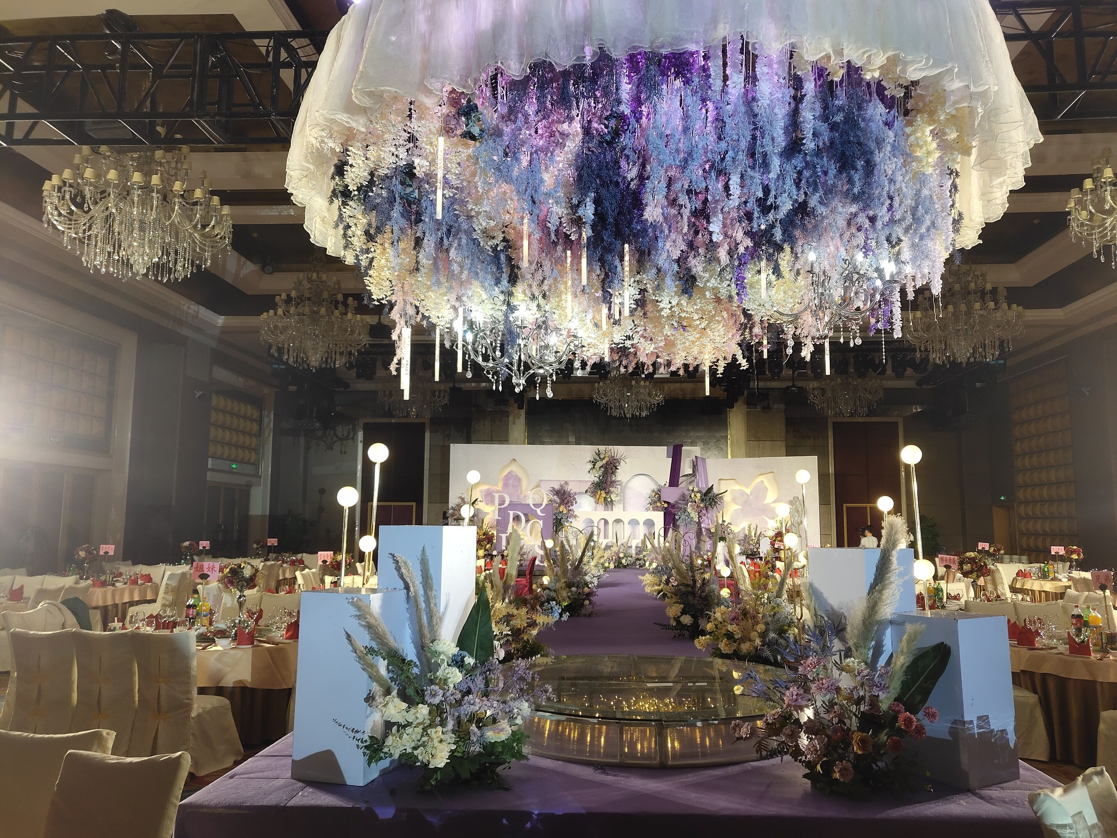 A banquet hall with a central stage, surrounded by tables set for a formal event.