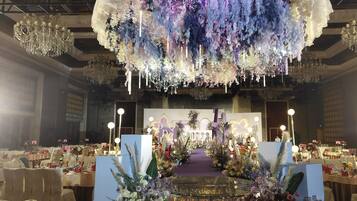 A banquet hall with a central stage, surrounded by tables set for a formal event.