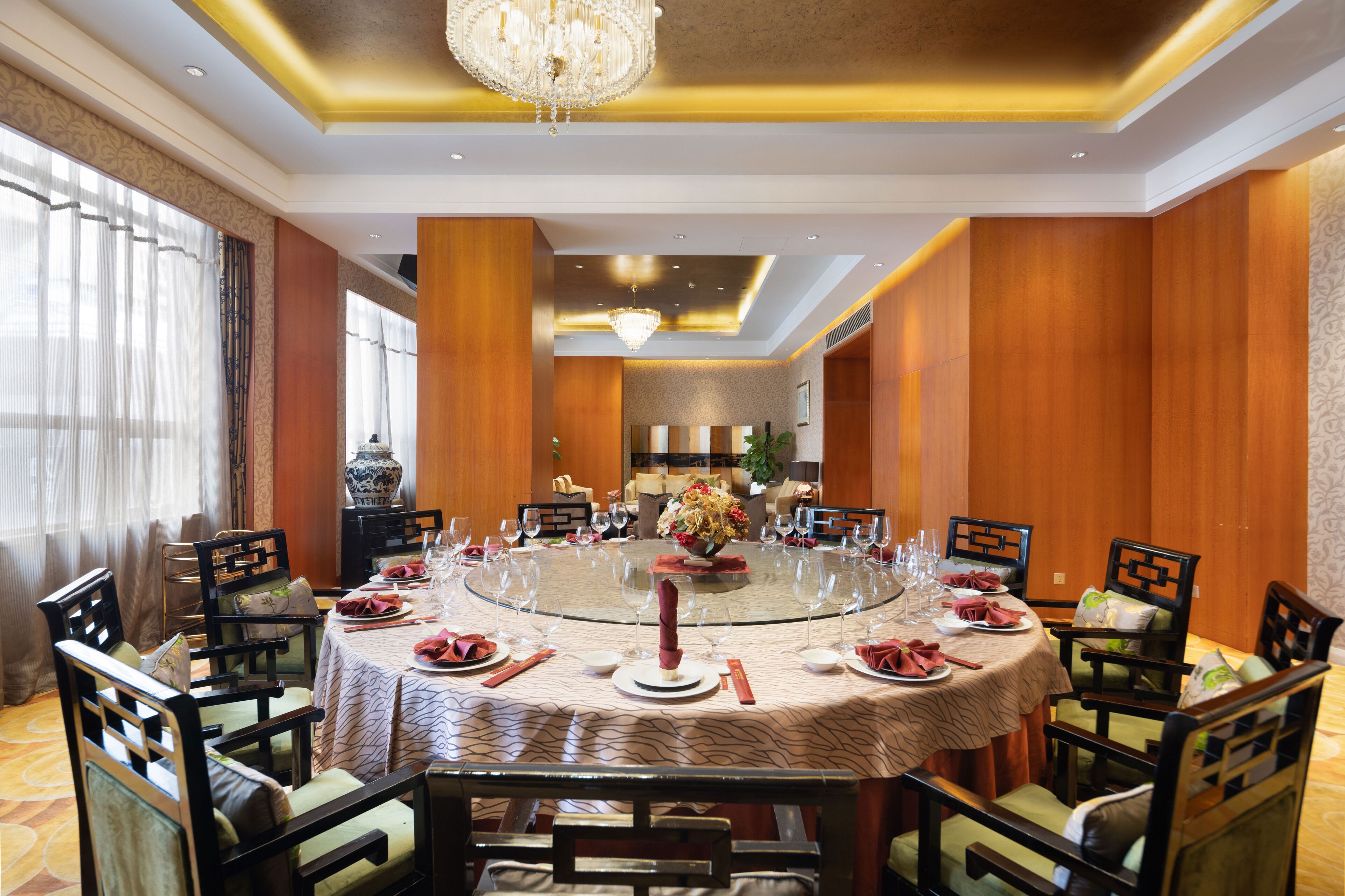 A round dining table with chairs, a chandelier, and a vase with flowers.