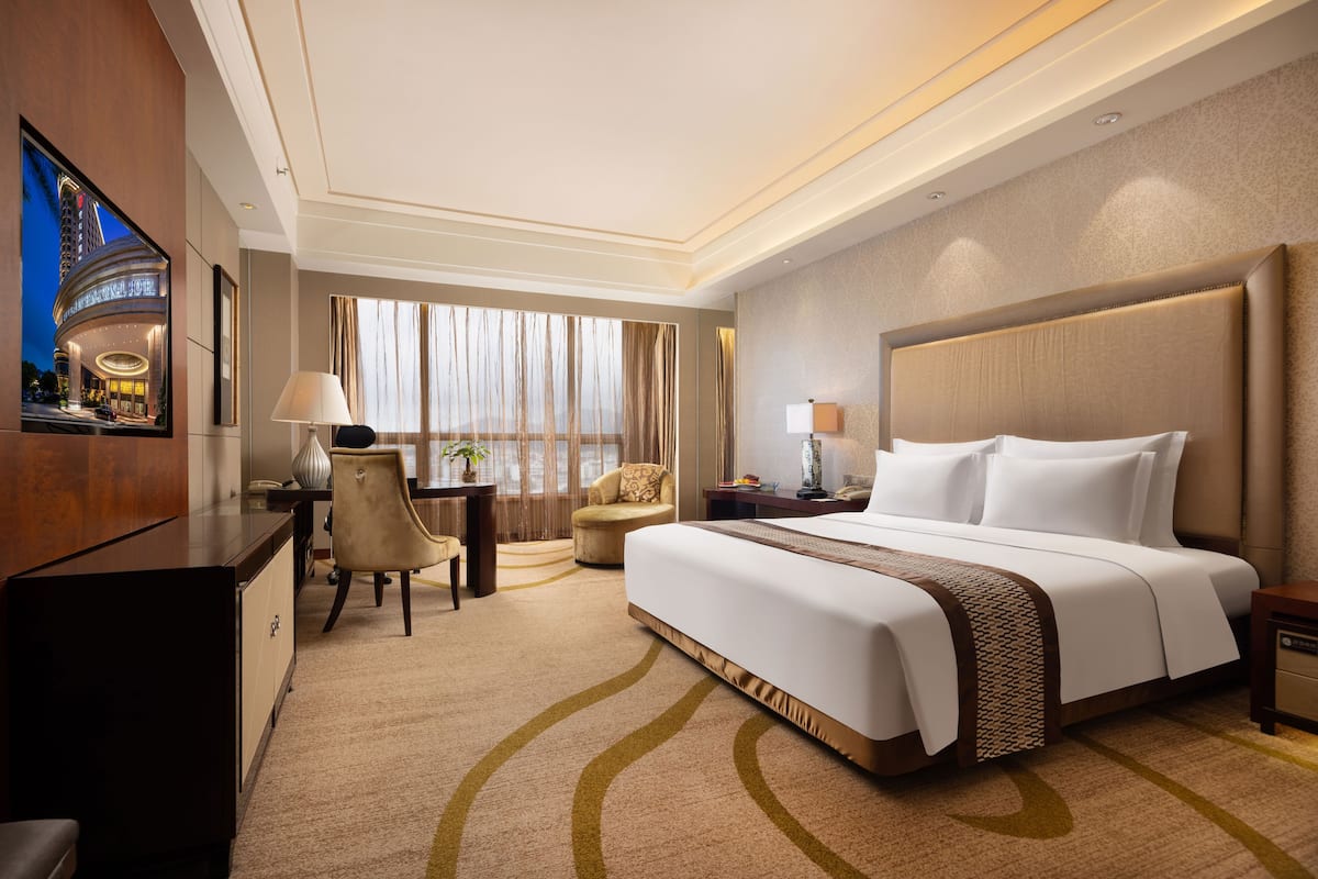 A hotel room with a large bed, a desk, a chair, and a TV mounted on the wall.