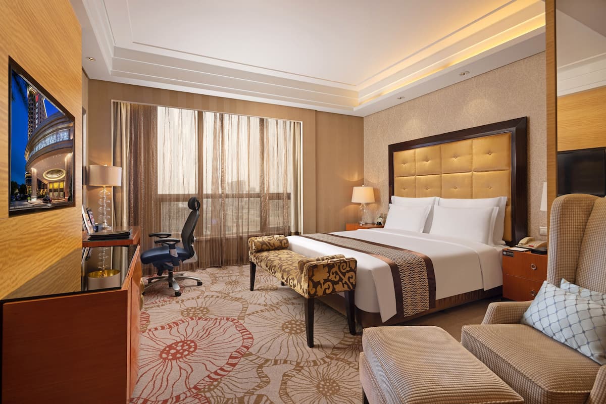A hotel room with a large bed, a desk with a lamp, a chair, and a television.